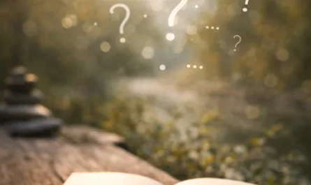 Ein aufgeschlagenes, leeres Notizbuch liegt auf einem rustikalen Holztisch inmitten einer ruhigen Naturlandschaft. Ein silberner Stift ruht diagonal auf den Seiten, bereit zum Schreiben. Im Hintergrund sind weiche, warme Lichtstrahlen der untergehenden Sonne zu sehen, die durch unscharfe Bäume und eine friedliche Umgebung scheinen. Über dem Notizbuch schweben mehrere halbtransparente Fragezeichen in unterschiedlichen Größen, die den Raum zwischen Denken und Nicht-Wissen symbolisieren. Im oberen Bereich des Bildes steht in klarer Schrift der Titel „Im Dazwischen entsteht Wirkung“. Die Gesamtstimmung ist ruhig, reflektierend und offen, als Einladung, Gedanken entstehen zu lassen, ohne sie sofort beantworten zu müssen.